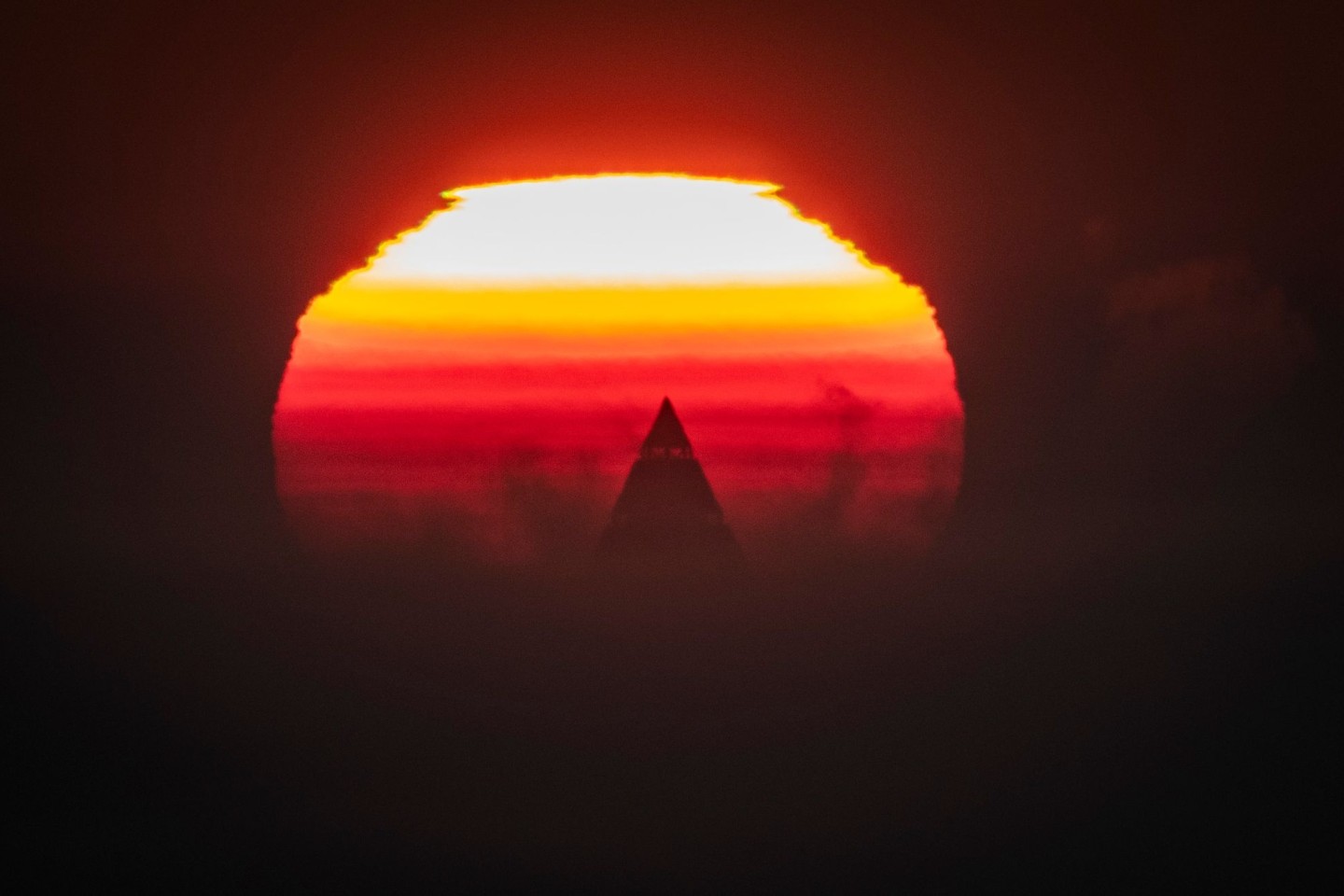 Die Spitze des Messeturms ragt als einziges Gebäude der Skyline von Frankfurt vor der aufgehenden Sonne heraus.
