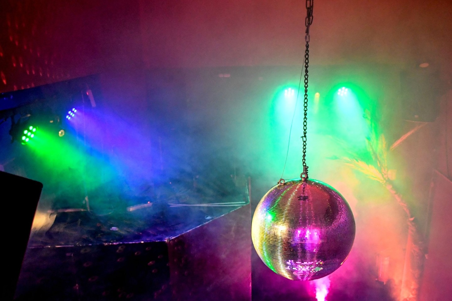 Eine Diskokugel dreht sich in einem Club und reflektiert das einfallende Licht der Scheinwerfer und Lampen.