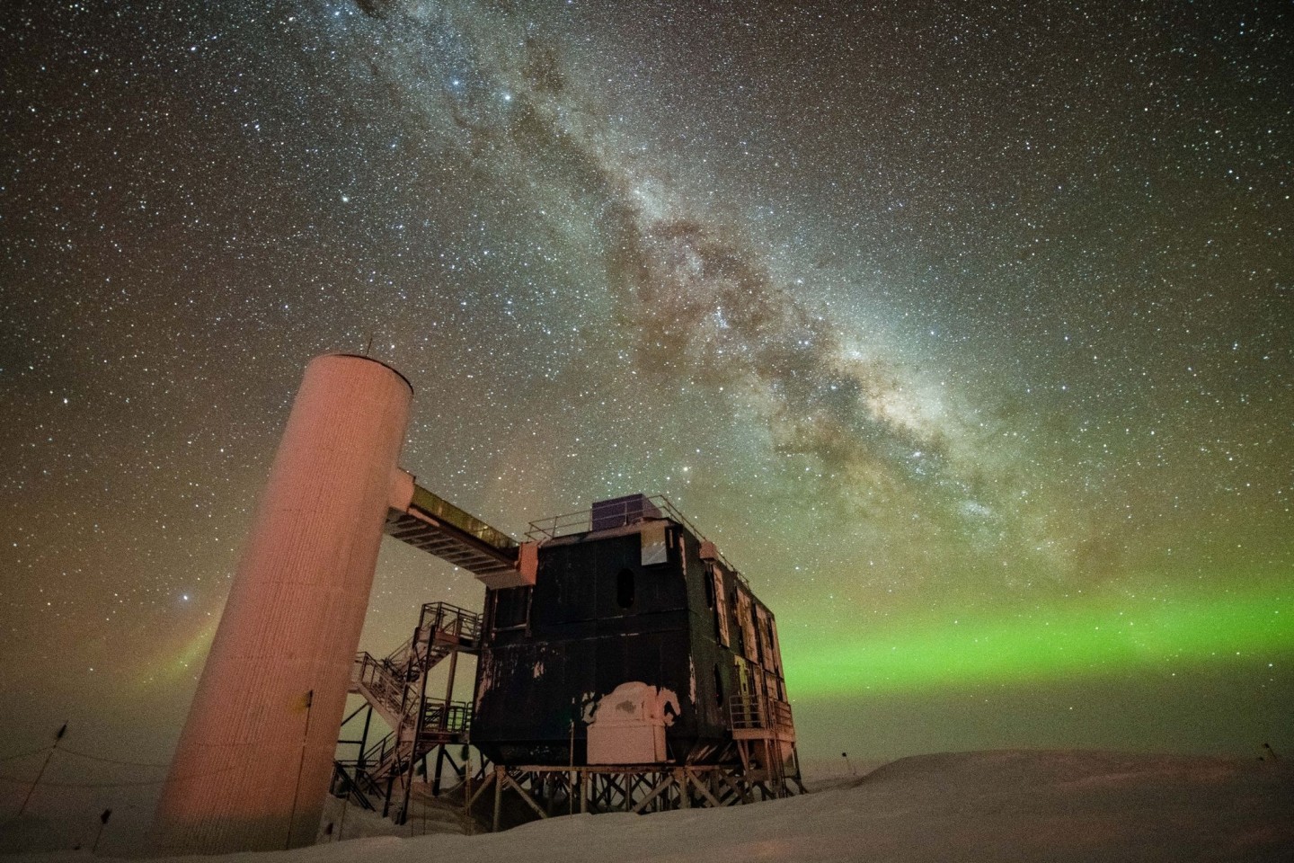 Blick auf das «IceCube»-Labor mit einem sternenklaren Nachthimmel, der die Milchstraße und grüne Polarlichter zeigt.