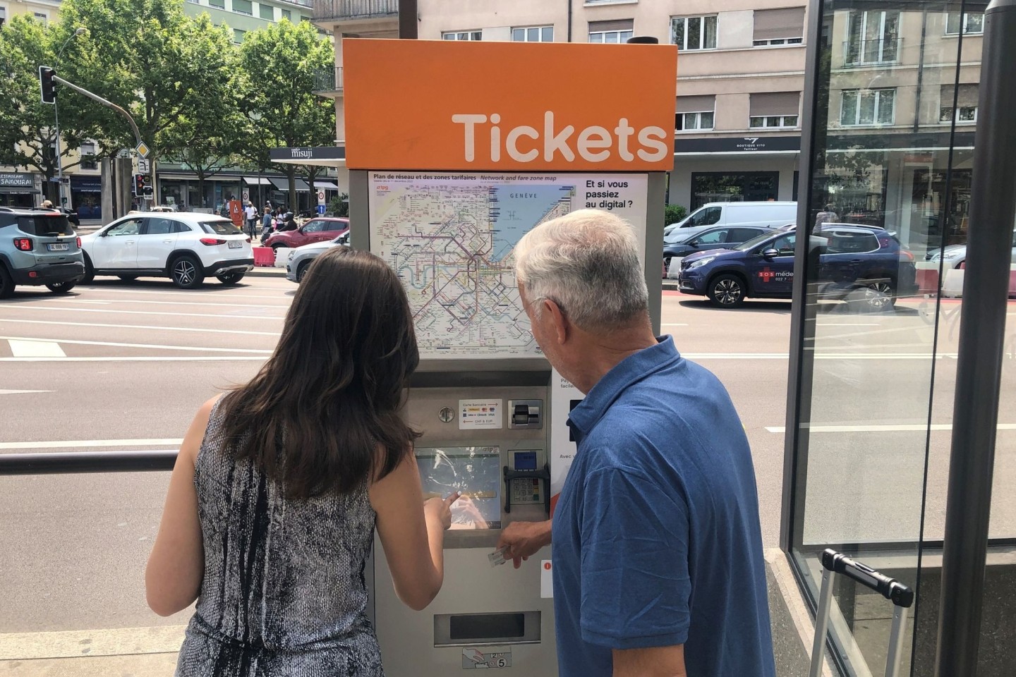 Zwei Leute versuchen, an einem Ticket-Automaten in Genf Fahrkarten zu erwerben.
