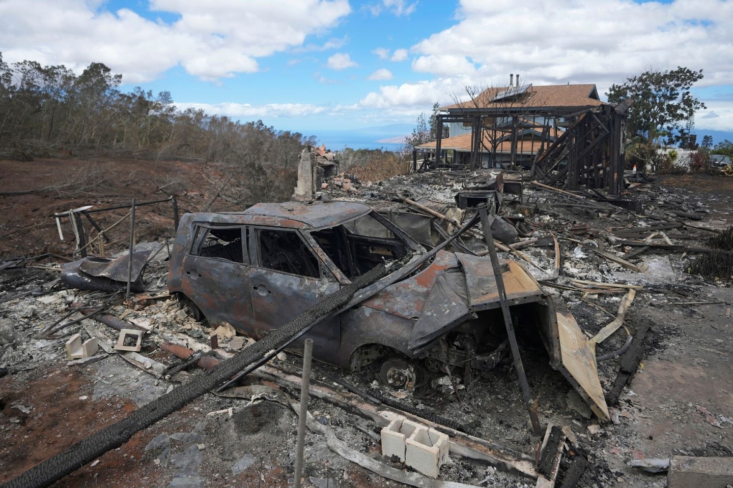 Die verkohlten Überreste eines Fahrzeugs stehen in Kula neben einem von einem Waldbrand zerstörten Haus.
