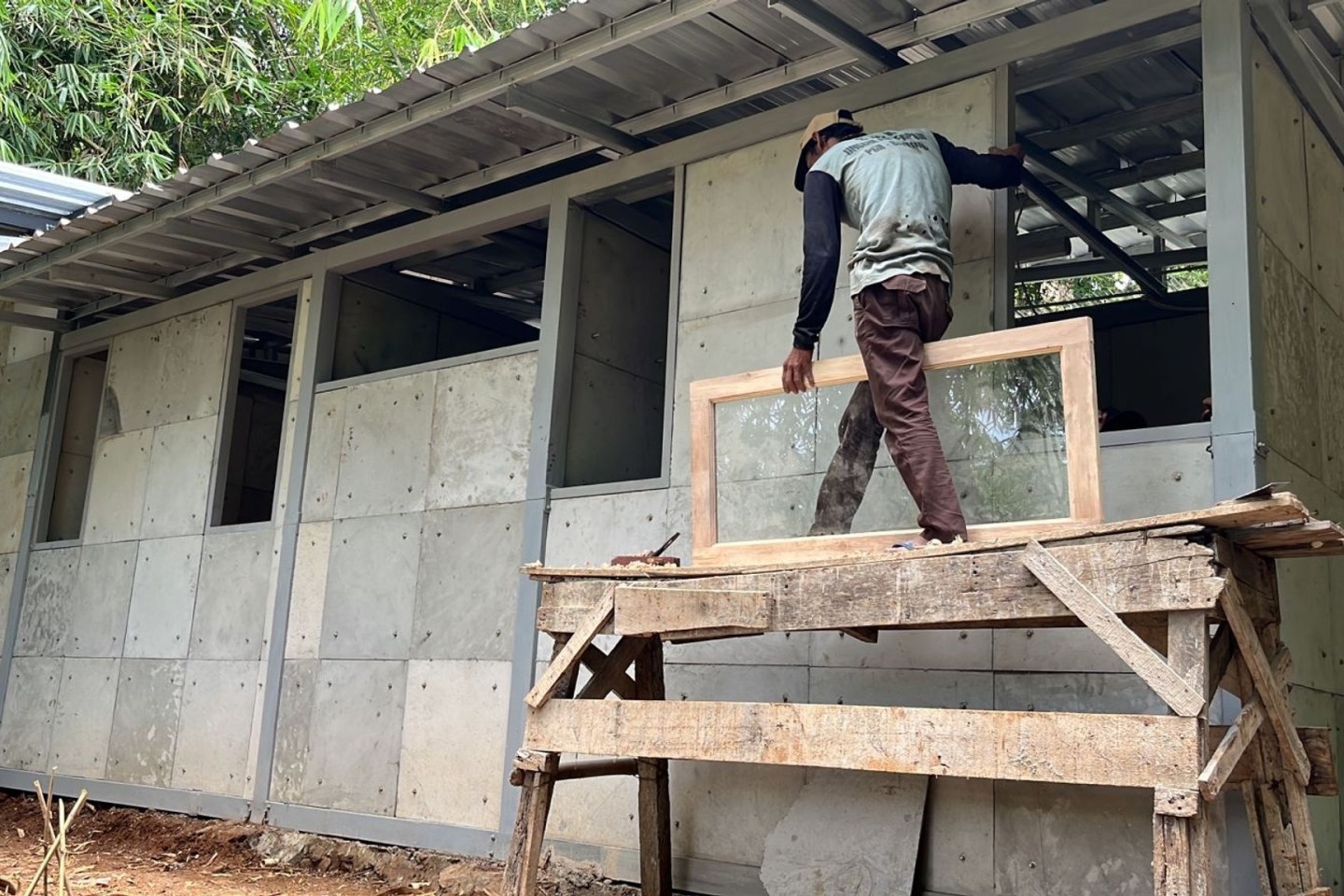 Ein Mann arbeitet am Rohbau eines einfachen Hauses, bei dem gebrauchte Windeln einen Teil des Baumaterials ersetzen.