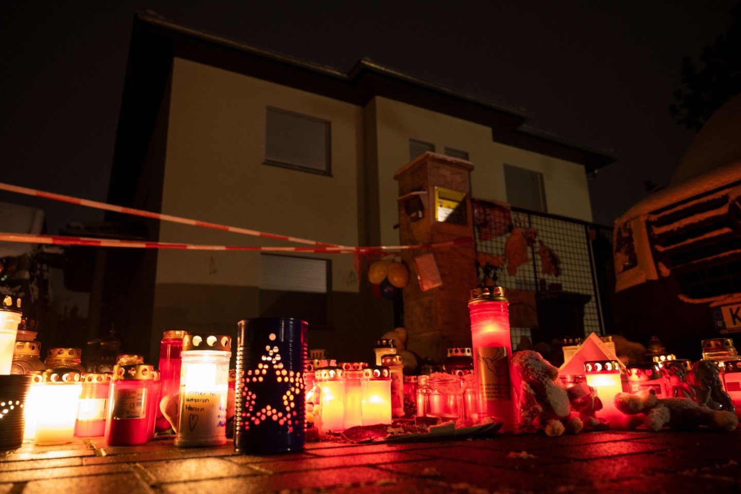 Kerzen brennen auf dem Gehweg vor dem Einfamilienhaus Königs Wusterhausen, wo Polizisten eine Familie tot aufgefunden hatten.