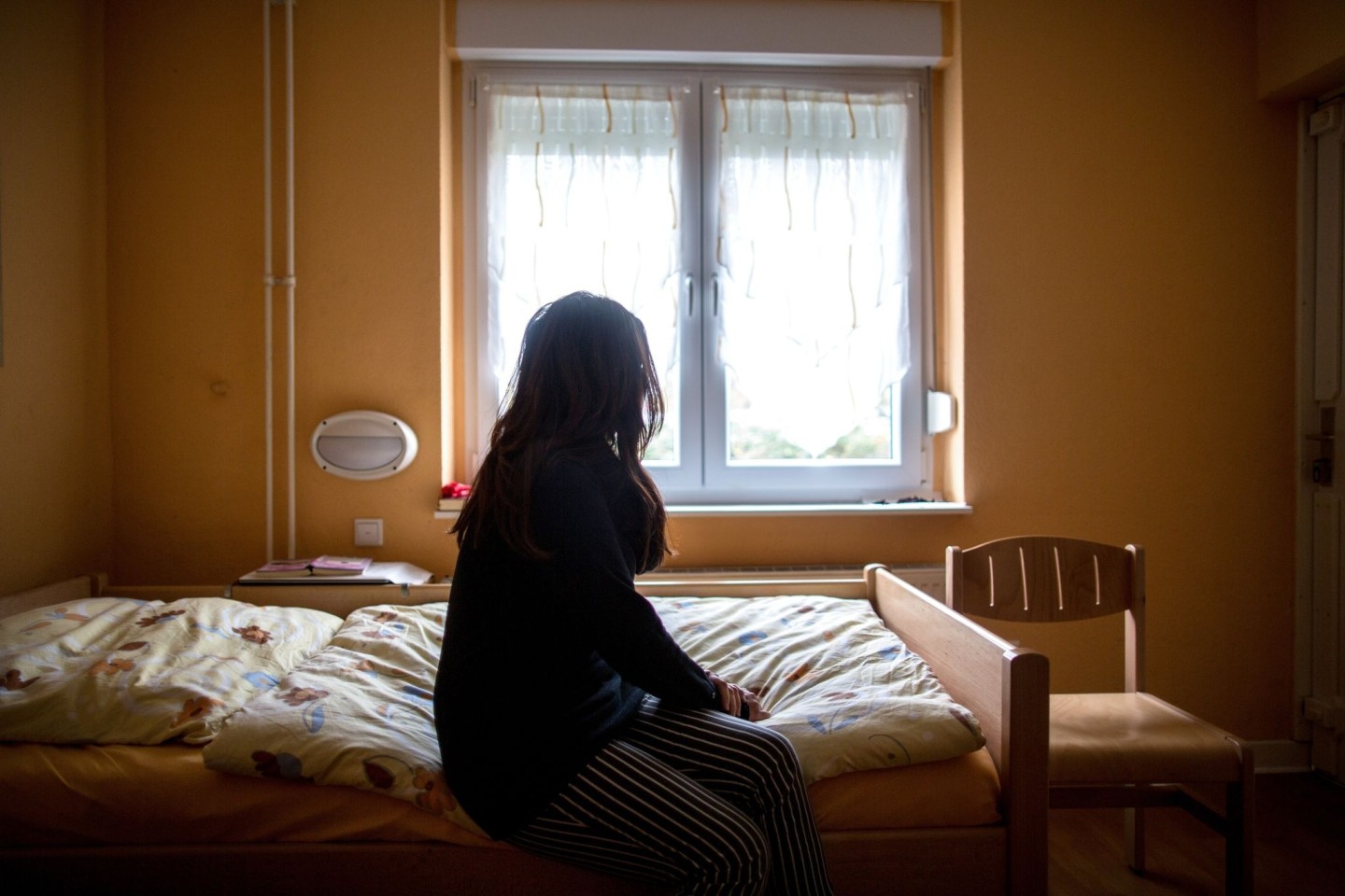 Eine Frau sitzt in einem Frauenhaus auf einem Bett.