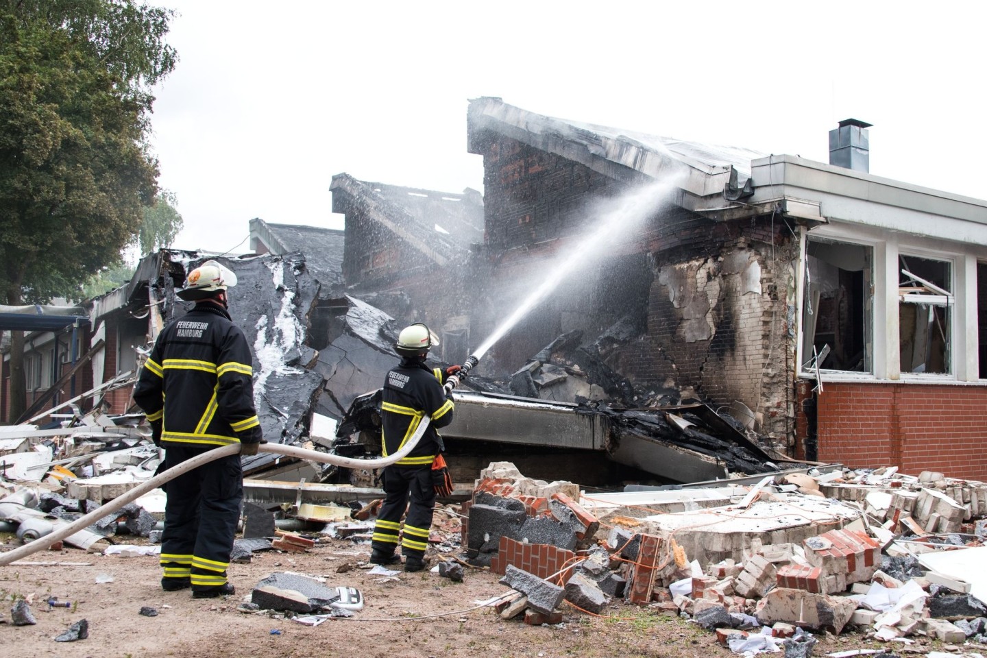 Feuerwehrleute löschen Trümmer eines Gebäudes der Stadtteilschule Finkenwerder.