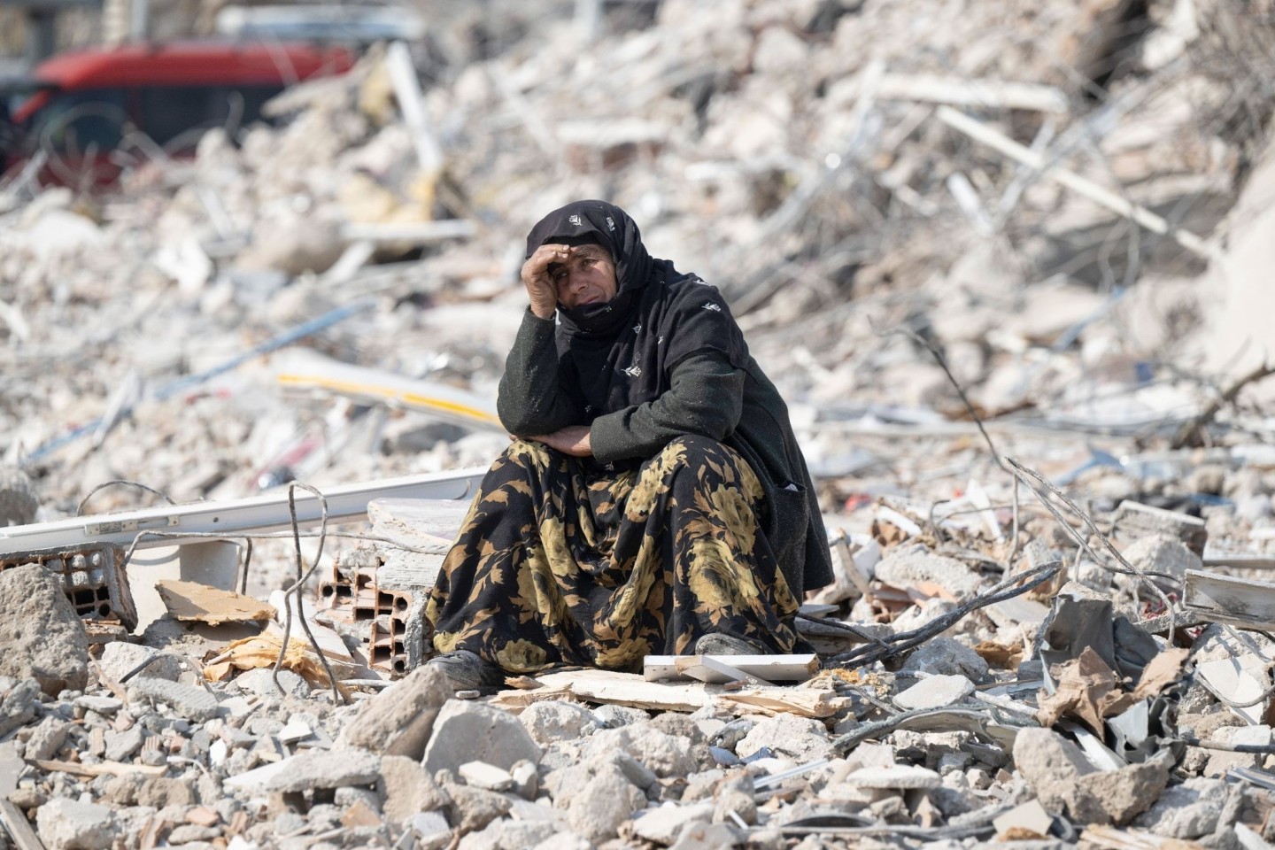 Eine Frau in Antakya beobachtet zwischen den Trümmern die Bergung von Opfern.