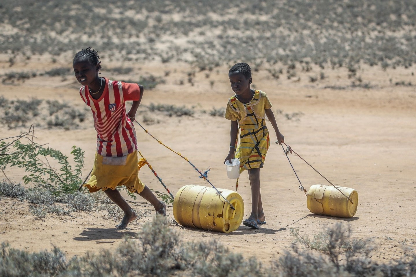 Zwei junge Mädchen ziehen in Kenia Wasserbehälter auf dem Rückweg zu ihren Hütten.