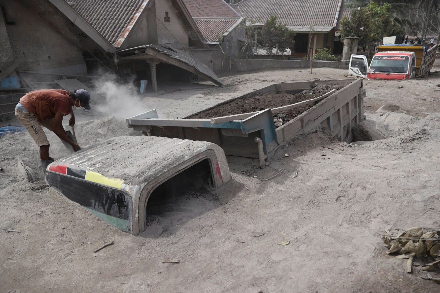Ein Mann inspiziert einen Lastwagen, der nach dem Ausbruch des Mount Semeru unter Vulkanasche begraben wurde.