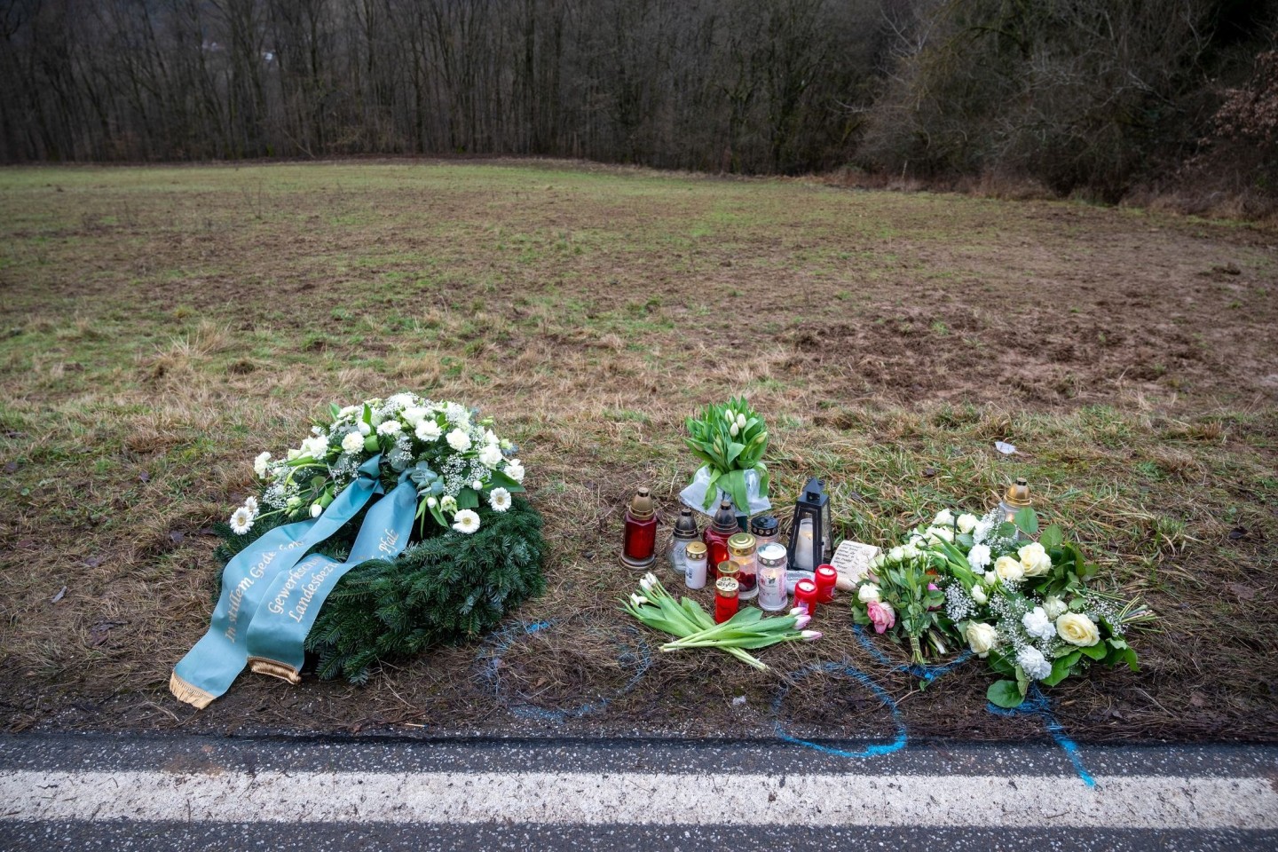 Ein Kranz sowie Blumen und Kerzen liegen am Tatort an der Kreisstraße 22 bei Ulmet (Rheinland-Pfalz).
