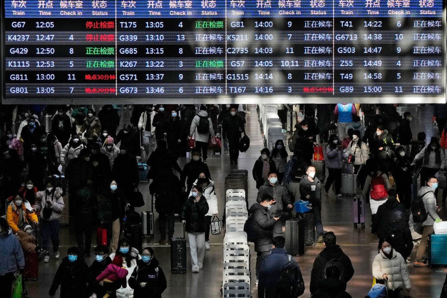 Reisende mit ihrem Gepäck gehen unter einer Zugabfahrtstafel am Westbahnhof in Peking.