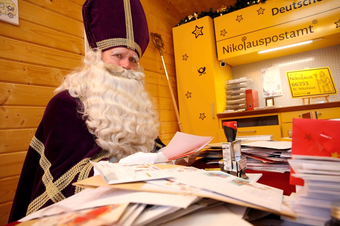 Ein als Nikolaus verkleideter Mann sitzt im Nikolauspostamt in St. Nikolaus vor vielen Briefen.