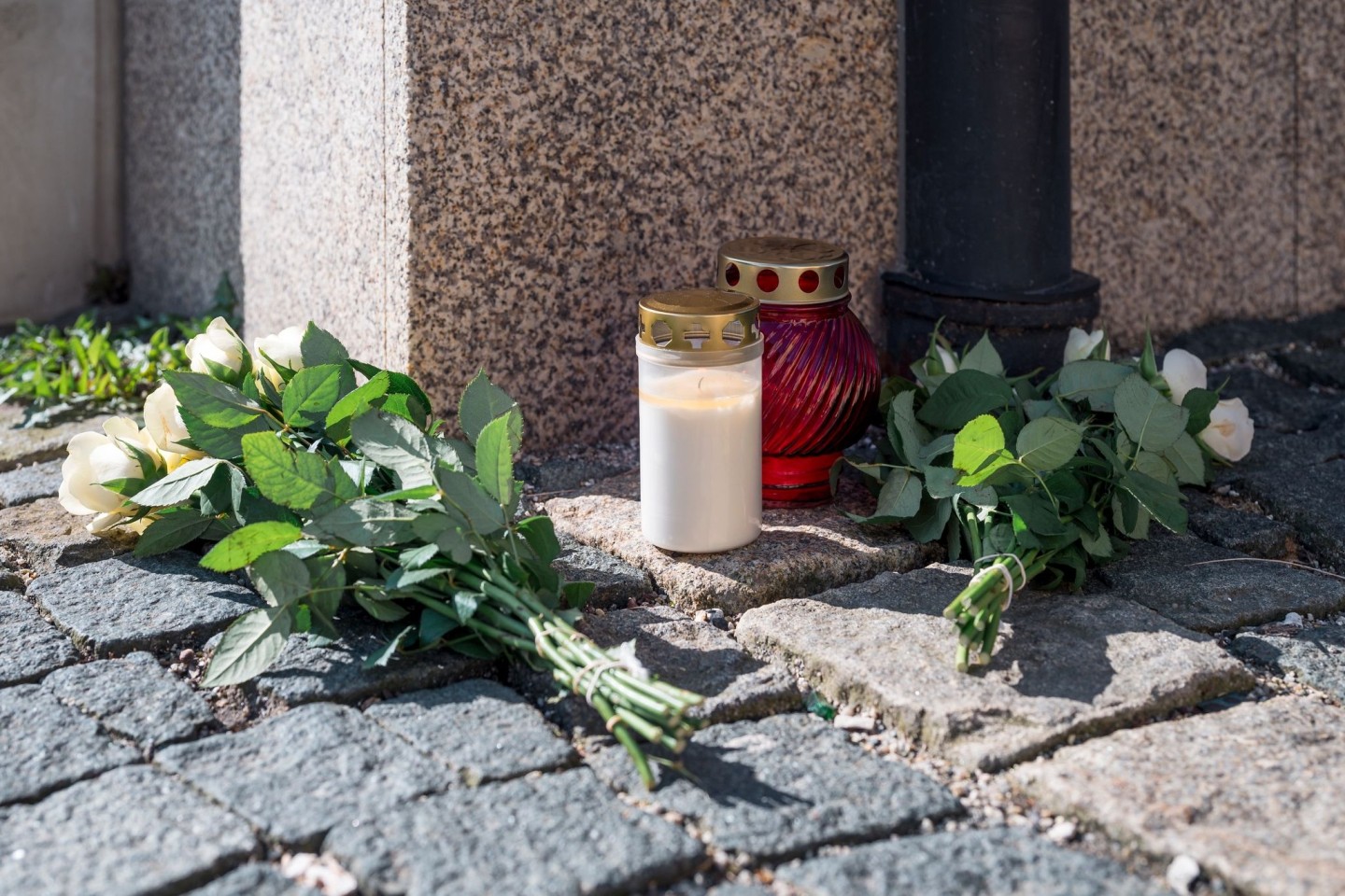An der Straßenecke zur Zufahrt zum Kinder- und Jugendhilfezentrum, in dem eine Zehnjährige tot aufgefunden wurde, liegen weiße Rosen und Grablichter auf dem Gehweg.