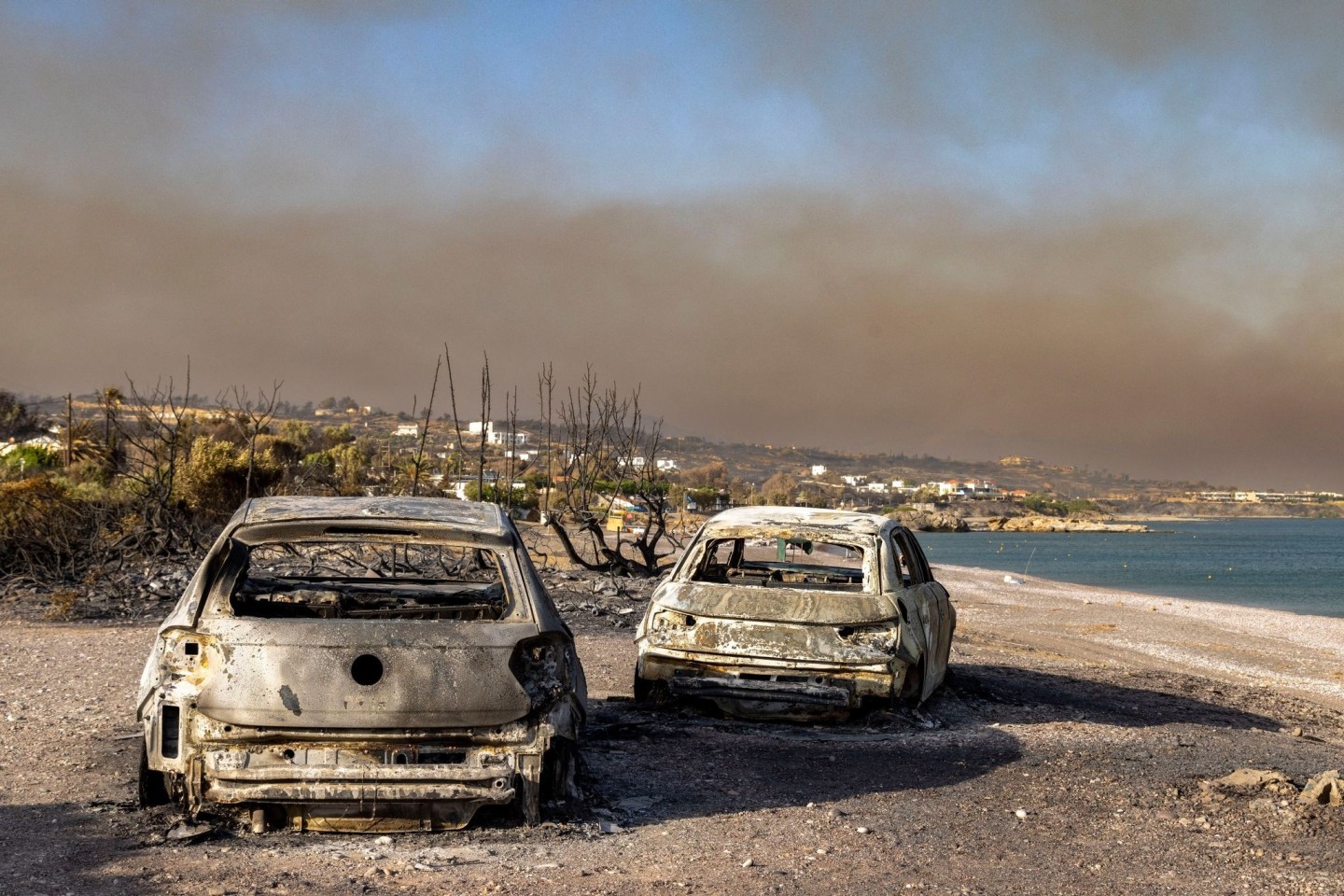 Ausgebrannte Autos am Strand von Kiotari. Im Hintergrund ist eine riesige Rauchwolke zu sehen.