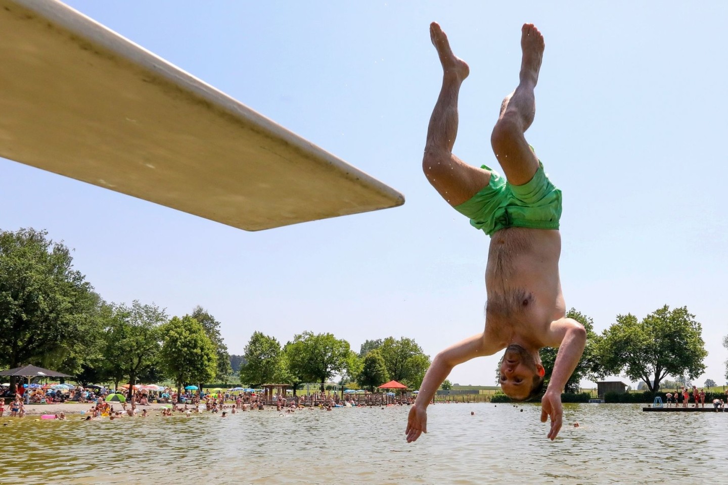 Hitze auch am Sonntag: Ein Mann springt kopfüber von einem Sprungbrett in das Wasser.