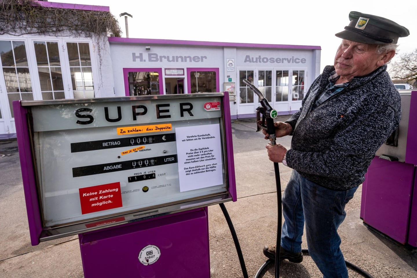 Hans Brunner steht an einer Zapfsäule seiner Tankstelle. Die Tankstelle zeigt Benzin- und Dieselpreise halbliterweise an.