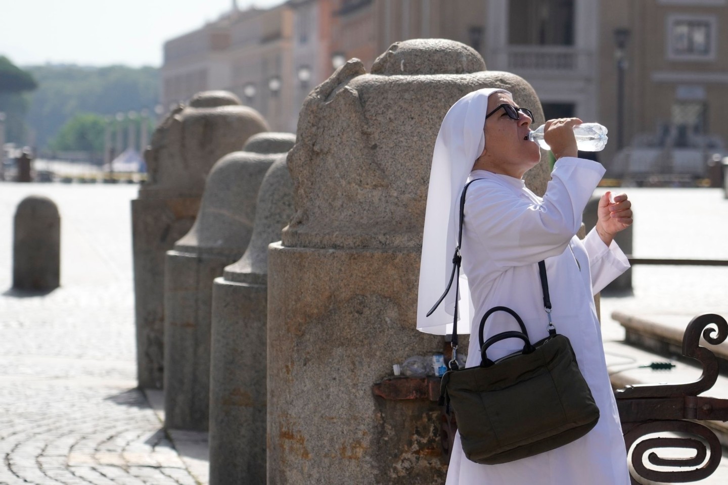 Eine Nonne erfrischt sich auf dem Petersplatz mit einem Schluck aus der Wasserflasche.