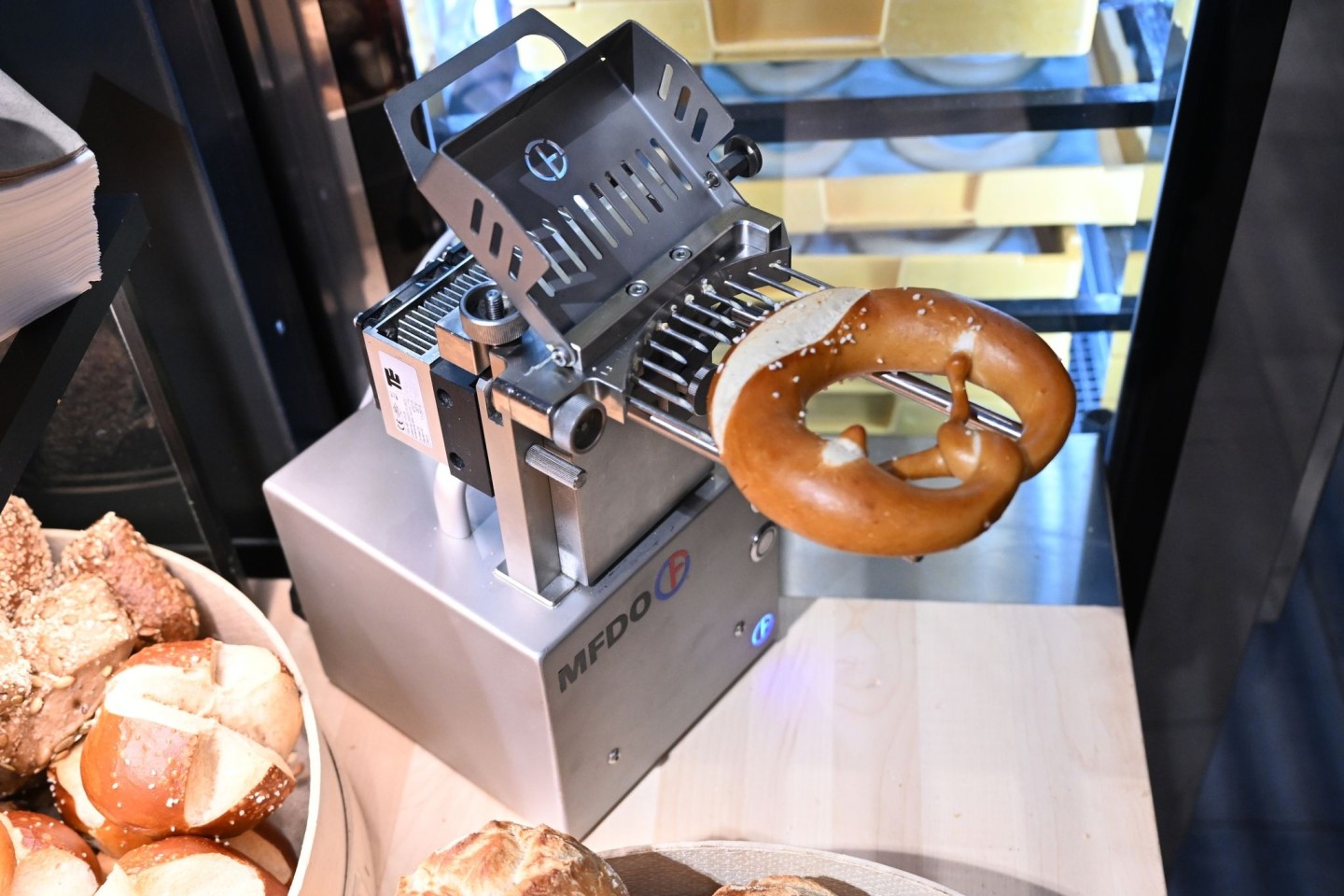 Eine Maschine befüllt in einer Bäckerei eine Brezel mit Butter.