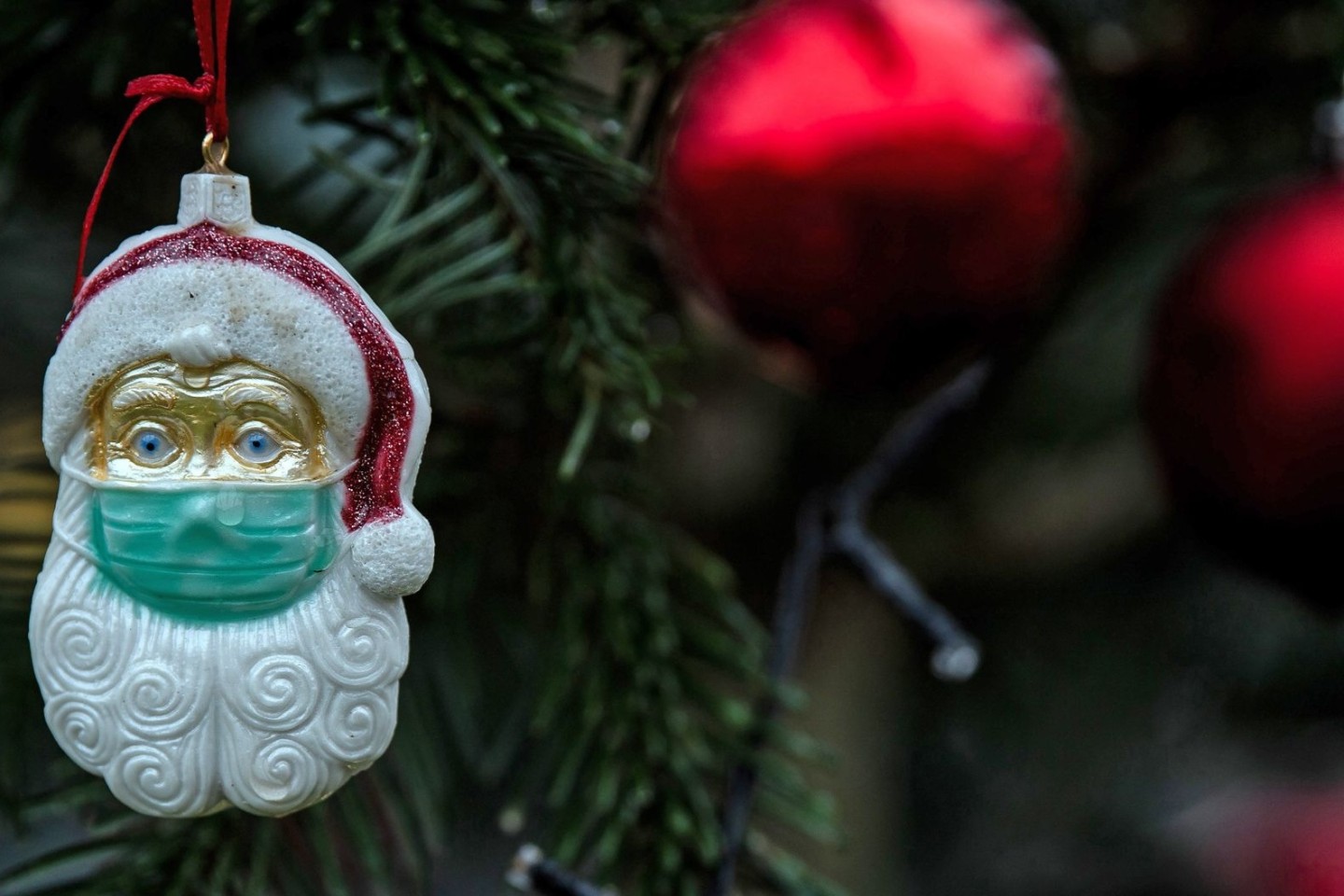 Ein Weihnachtsmann mit einer Schutzmaske hängt als Weihnachtsbaumschmuck in einem Tannenbaum.