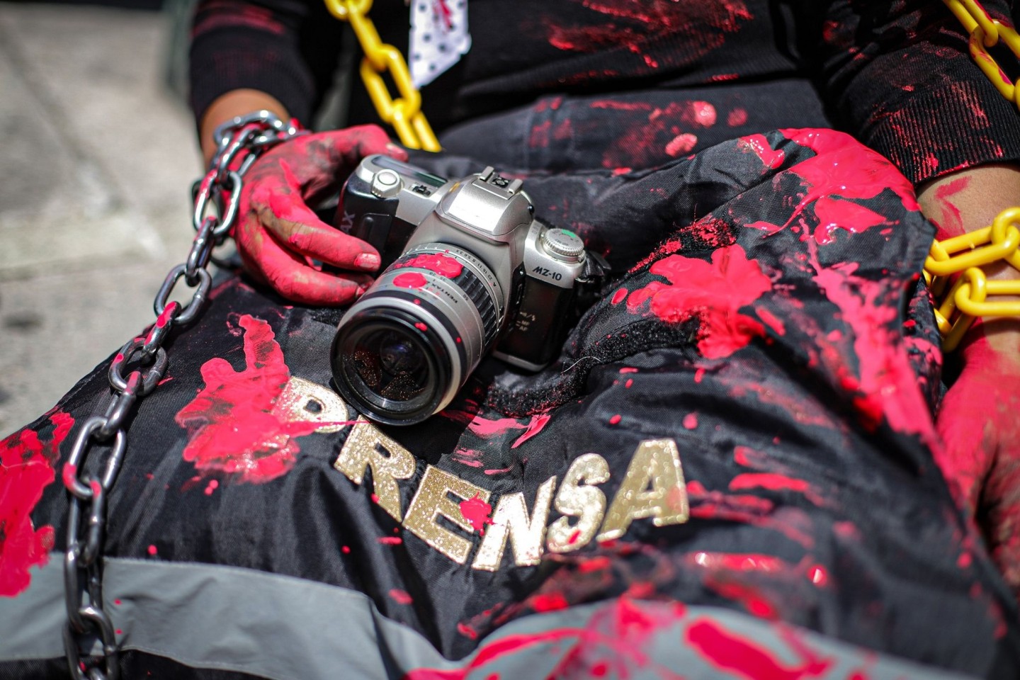 Eine Journalistin und Aktivistin mit einer rot verschmierten Kamera und einer Presseweste bei einer symbolischen Aktion in Mexiko-Stadt.