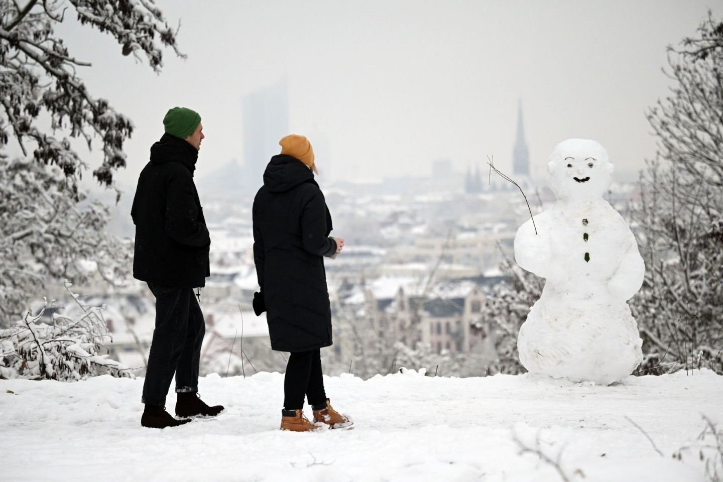 Zwei Spaziergänger wandern am Fockeberg (Leipzig) an einem Schneemann vorbei.